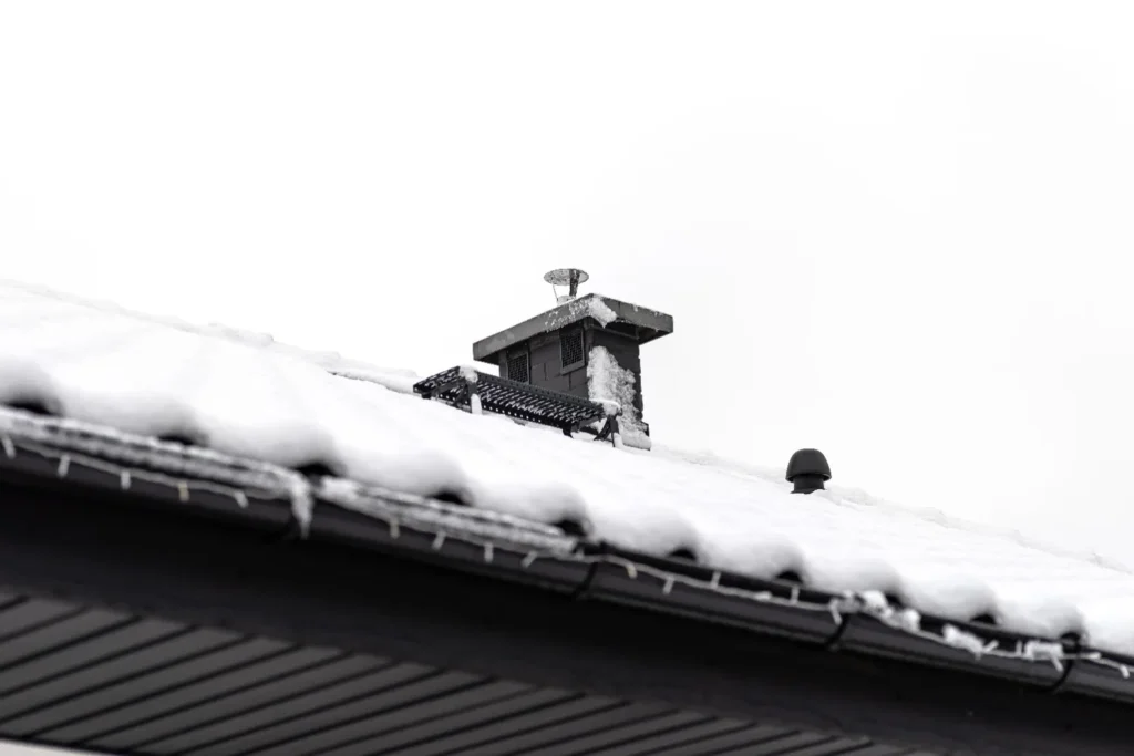 Snow-covered roofs with chimney and vents during winter weather