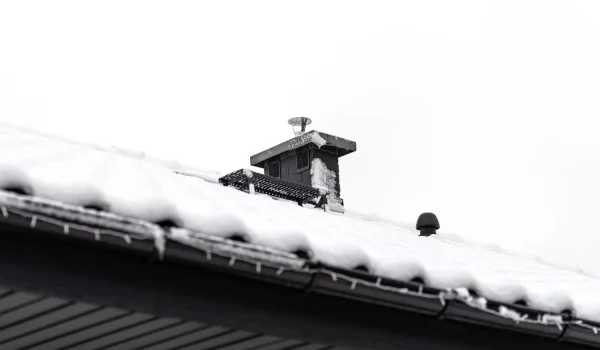 Snow-covered roofs with chimney and vents during winter weather